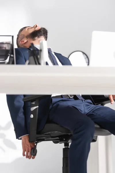 Empresário exausto olhando para longe perto do laptop em primeiro plano desfocado — Fotografia de Stock