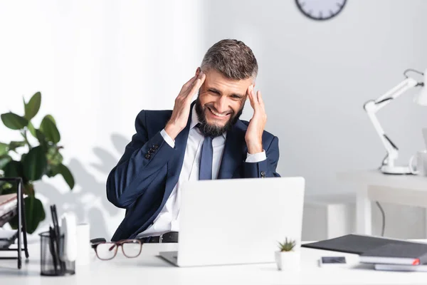 Homme d'affaires souffrant de maux de tête près d'un ordinateur portable et des papiers sur la table de travail — Photo de stock