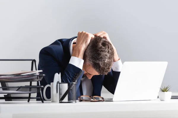 Homem de negócios cansado sentado perto do laptop e documentos em primeiro plano desfocado no escritório — Fotografia de Stock