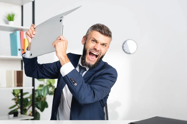 Angry businessman screaming while holding laptop in office — Stock Photo