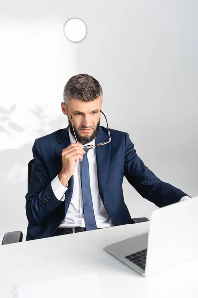 Businessman with eyeglasses using laptop on blurred foreground in office — Stock Photo