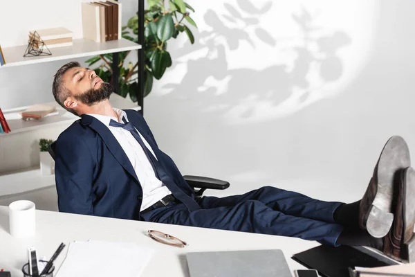 Businessman sleeping near gadgets and stationery on blurred foreground in office — Stock Photo