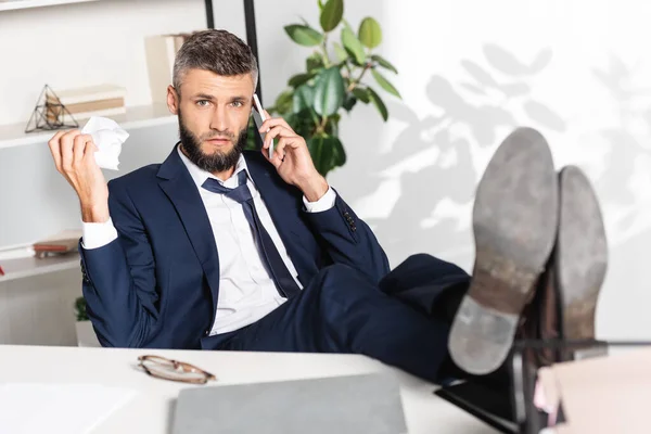 Nervous businessman holing clumped paper while talking on smartphone while working in office — Stock Photo