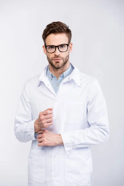 Visão frontal do médico sério em óculos segurando mangas de camisa, enquanto olha para a câmera isolada no branco — Fotografia de Stock