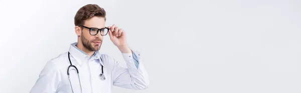 Confident doctor with stethoscope holding eyeglasses frame, while looking at camera on grey background, banner — Stock Photo