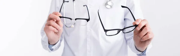 Vista recortada del oftalmólogo sosteniendo un par de gafas con monturas negras aisladas en blanco, pancarta - foto de stock