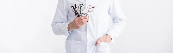 Cropped view of doctor with hand in pocket holding several eyeglasses isolated on white, banner — Stock Photo