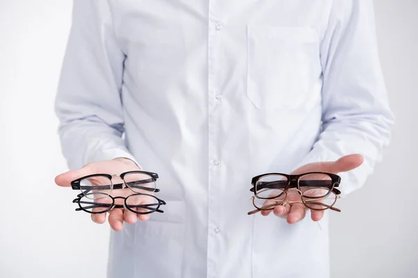 Vista recortada del médico mostrando pares de anteojos en palmas aisladas en blanco - foto de stock