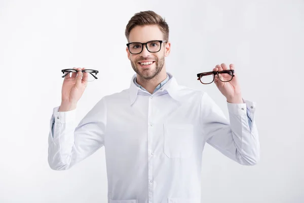 Front view of cheerful ophthalmologist with hands in air showing pair of eyeglasses, while looking at camera isolated on white — Stock Photo