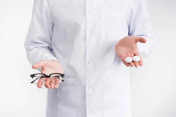 Cropped view of ophthalmologist holding on palms lenses container higher than eyeglasses isolated on white — Stock Photo