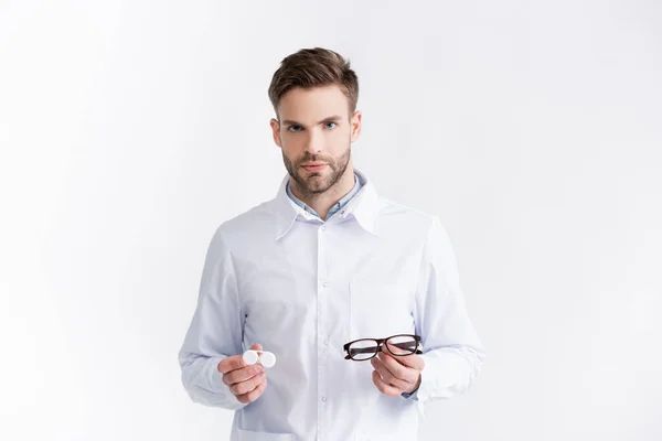 Front view of confident ophthalmologist showing eyeglasses and lenses container, while looking at camera isolated on white — Stock Photo