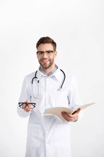 Vue de face du médecin souriant avec stéthoscope tenant lunettes et dossier isolé sur blanc — Photo de stock