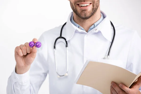 Обрезанный вид улыбающегося офтальмолога со стетоскопом, держащим папку и показывающим контейнер для линз, изолированный на белом — стоковое фото