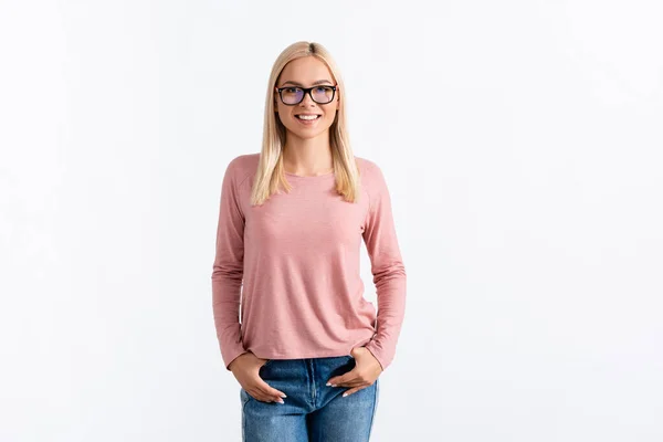 Front view of happy blonde woman with hands in pockets, wearing eyeglasses and looking at camera isolated on white — Stock Photo