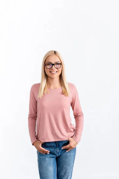 Front view of smiling blonde woman with hands in pockets, wearing eyeglasses and looking at camera isolated on white — Stock Photo