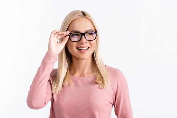 Happy blonde woman in pink long sleeve holding eyeglasses frame, while looking away isolated on white — Stock Photo