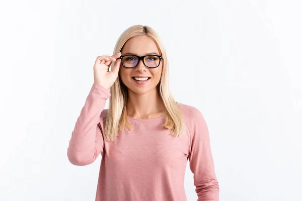 Visão frontal da mulher loira feliz na manga comprida rosa segurando quadro de óculos, enquanto olha para a câmera isolada no branco — Fotografia de Stock