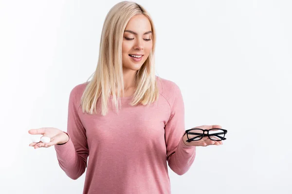 Mulher loira sorrindo enquanto segura óculos e contêiner com lentes de contato isoladas em branco — Fotografia de Stock