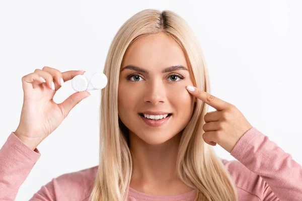 Lächelnde Frau zeigt mit dem Finger auf Auge und hält Schachtel mit Kontaktlinsen isoliert auf weiß — Stockfoto