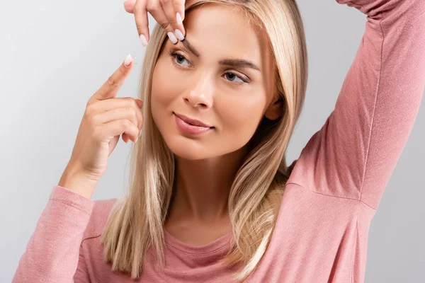 Femme blonde mettant lentille de contact dans l'œil isolé sur gris — Photo de stock