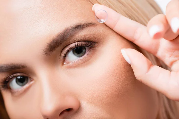 Ausgeschnittene Ansicht einer Frau, die in die Kamera schaut, während sie Kontaktlinse isoliert auf Weiß hält — Stockfoto