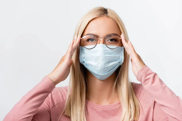Mujer joven en máscara médica tocando gafas aisladas en gris - foto de stock
