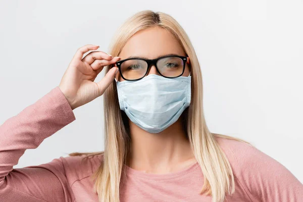 Mujer joven con máscara médica y anteojos empañados mirando a la cámara aislada en gris - foto de stock