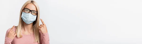Blonde Frau in medizinischer Maske, die auf eine vernebelte Brille zeigt, die auf einem grauen Banner isoliert ist — Stockfoto