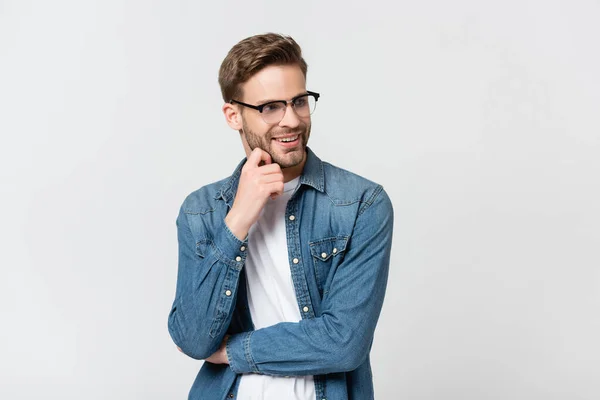 Jeune homme aux lunettes souriant en regardant loin isolé sur gris — Photo de stock