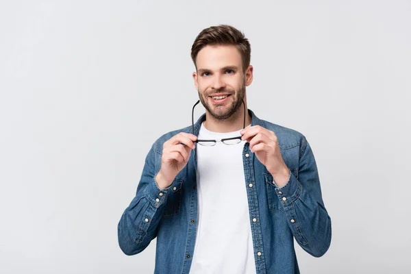 Hombre positivo mirando a la cámara mientras sostiene las gafas aisladas en gris - foto de stock