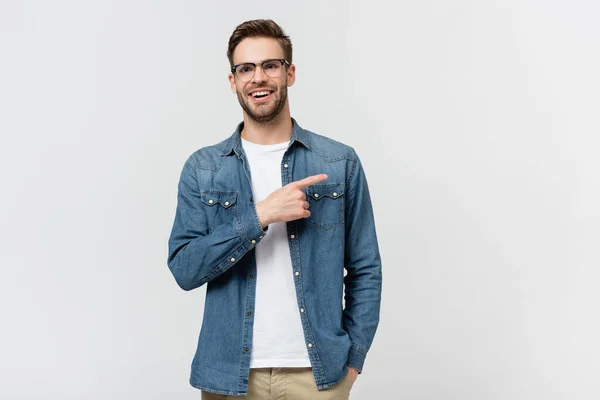 Hombre positivo en anteojos apuntando con el dedo lejos aislado en gris - foto de stock