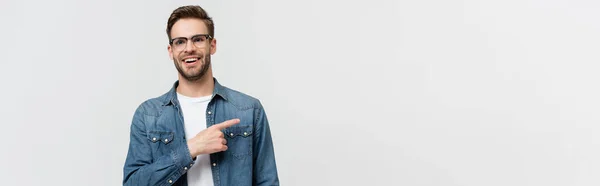 Hombre sonriente con anteojos apuntando con el dedo lejos aislado en gris, bandera - foto de stock