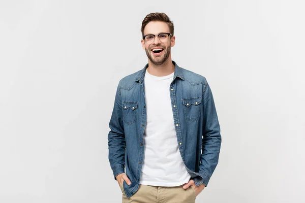 Uomo positivo in occhiali che si tiene per mano in tasche di pantaloni e distogliendo lo sguardo isolato sul grigio — Foto stock