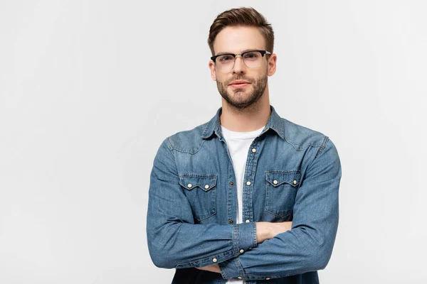 Jeune homme en lunettes regardant la caméra debout avec les bras croisés isolés sur gris — Photo de stock