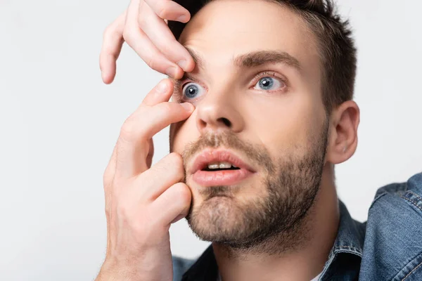 Young man putting contact lens in eye isolated on grey — Stock Photo