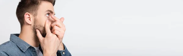 Чоловік торкається щоки під час носіння контактного лінзи ізольовано на сірому, банер — стокове фото