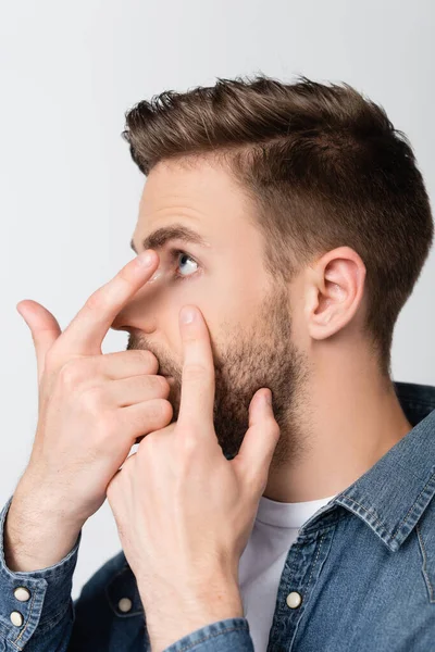 Giovane uomo che distoglie lo sguardo mentre indossa lenti a contatto isolate su grigio — Foto stock