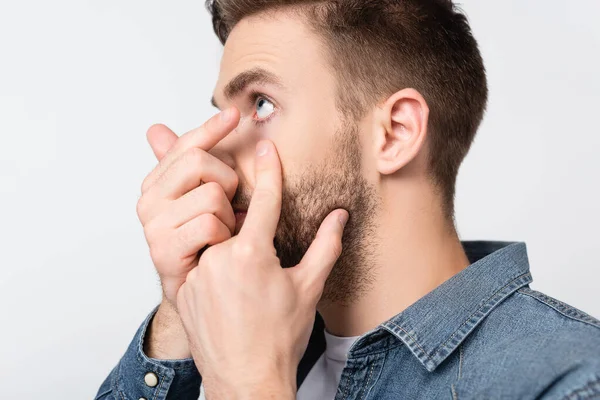 Giovane uomo con lente a contatto e guancia toccante isolato su grigio — Foto stock