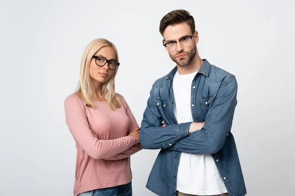 Молода пара в окулярах дивиться на камеру, стоячи з схрещеними руками ізольовані на сірому — стокове фото