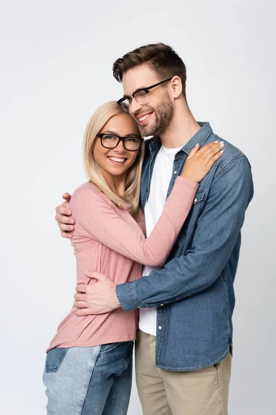 Young man in eyeglasses smiling while embracing girlfriend isolated on grey — Stock Photo