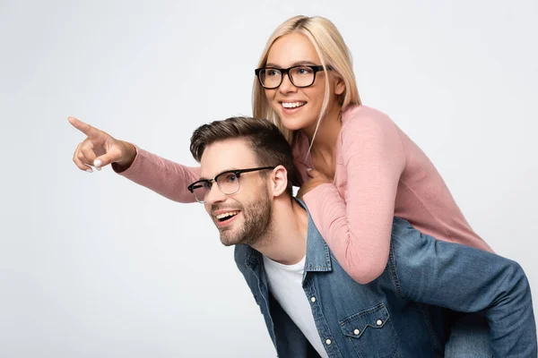 Mujer sonriente en gafas graduadas señalando con el dedo mientras se arrastra en novio aislado en gris — Stock Photo