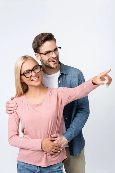 Smiling woman in eyeglasses pointing with finger near boyfriend isolated on grey — Stock Photo