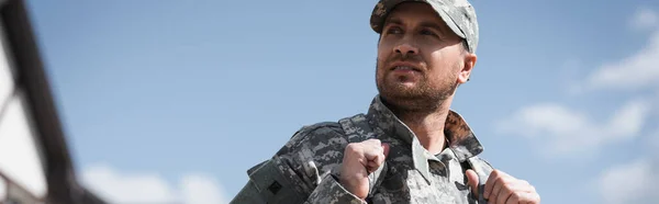 Serious military serviceman with backpack looking away with blurred sky on background, banner — Stock Photo