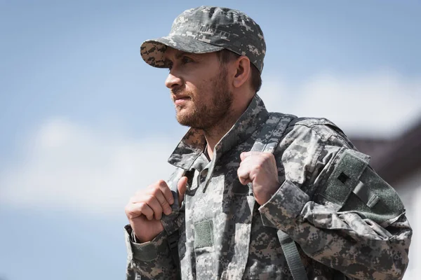 Soldat adulte en uniforme avec sac à dos regardant loin sur fond flou — Photo de stock