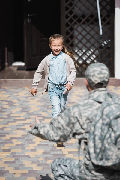 Счастливая девушка бежит, с размытым отцом в военной форме на переднем плане — стоковое фото