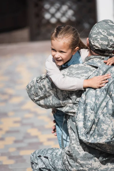 Vista trasera del militar abrazando a su hija sonriente sobre un fondo borroso - foto de stock