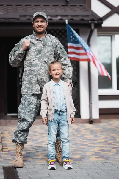 Vista frontal del padre en uniforme militar de pie con su hija sobre fondo borroso - foto de stock