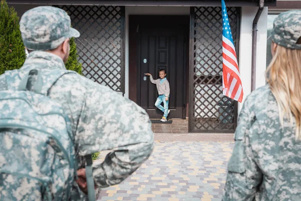 Girl standing on threshold with blurred military couple on foreground — Stock Photo