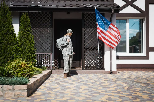 Военная женщина с рюкзаком выходит из дома, стоит на пороге — стоковое фото