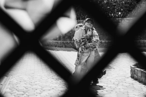 Mãe de uniforme militar abraçando filha com rede borrada em primeiro plano, monocromática — Fotografia de Stock